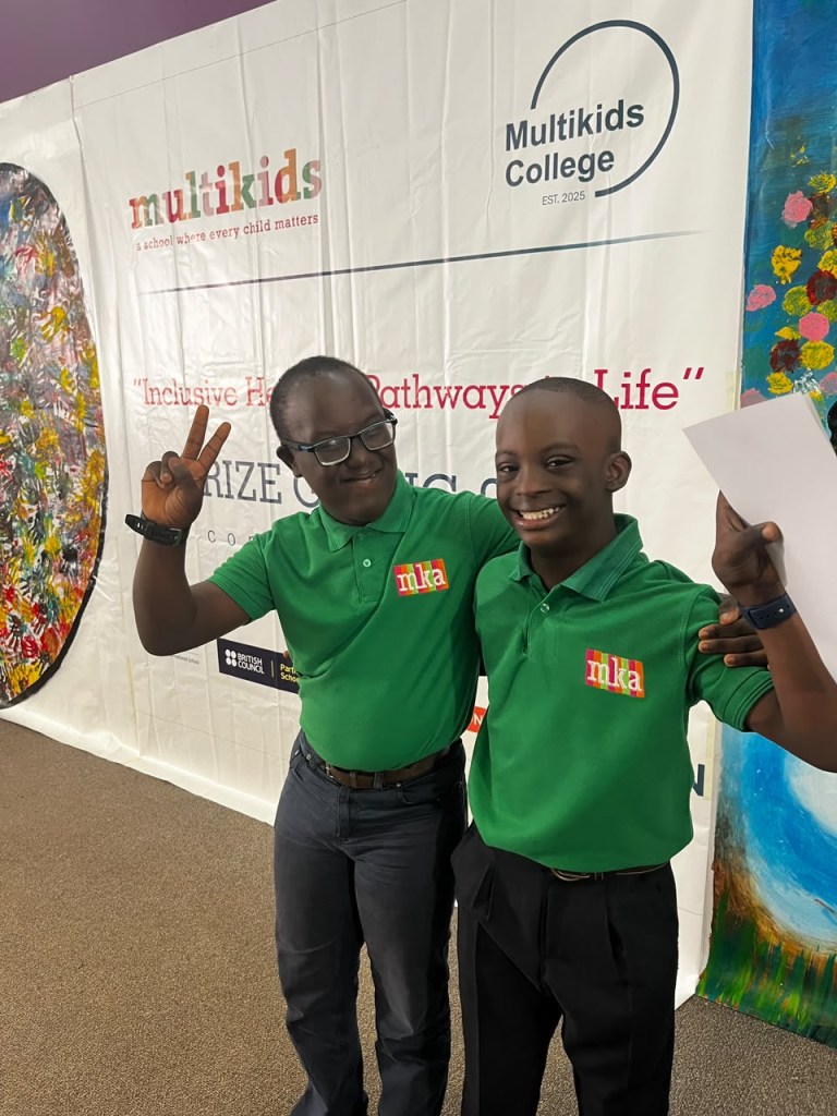 KEY and his classmate Theodore in green school polo shirts, arms around each other and smiling, in front of a Multikids banner. Theodore makes the peace sign.